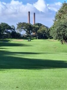 Golfer on the fairway at Rondebosch Golf Club with the old power station twin chimneys visible above the trees, MP 3, May 2026.